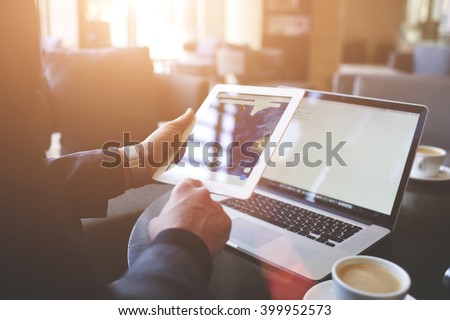 Male trader is searching information on web pages via portable digital tablet. Closeup of touch pad in man`s hand and laptop computer with copy space on the screens for your advertising text message.