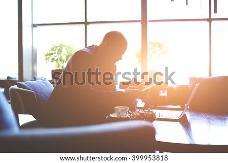Silhouette of man lawyer is preparing for court hearing, while is sitting with net-book and touch pad in office interior. Male managing director is analyzes activity of company by using digital tablet