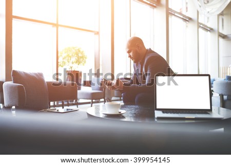 Man proud CEO is ordering on-line via cell telephone car for business trip, while is sitting in co-working cafe near table with open laptop computer with empty copy space screen for your advertising