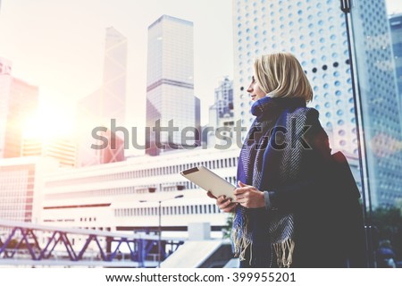 Young beautiful woman with portable touch pad in hands is enjoying view of New York business center outside the window background with copy space for advertising text message or promotional content