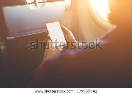 Closeup of man`s hands is holding mobile phone with empty copy space screen for your advertising text message or content.Hipster guy is reading electronic book on cell telephone during flying in plane