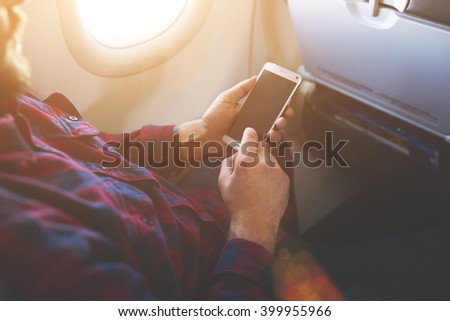 Closely image of a man`s hands is holding cell telephone with empty screen background for your advertising content. Closeup of male is watching photos on mobile phone while flying in an airplane