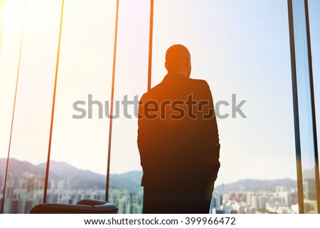 Silhouette of man managing director is examining the challenges the company after the refusal of investors in financing, while standing in evening time against office window background with copy space