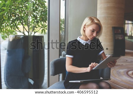 Young elegant female skilled managing director is reading e-mail on digital tablet positive feedback from the client about her work, while is sitting in luxury restaurant interior during break at job