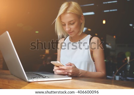 Beautiful lady chatting on smart phone while sitting at the table with laptop computer in cafe bar interior, pretty European woman using cell telephone while relaxing after work on portable net-book