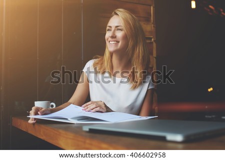 Beautiful female with cute smile looking away while relaxing after work on her laptop computer, charming happy woman enjoying rest and good day while sitting alone in modern coffee shop interior