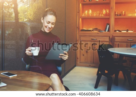 Young woman talking in video chat with her sister via digital tablet while sitting in her favorite cafe and drink delicious green tea, female watching movie on touch pad while breakfast in coffee shop