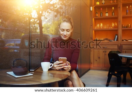 Portrait of young businesswoman use mobile phone while sitting in comfortable coffee shop during work break, charming happy female reading fashion news on cell telephone during breakfast in restaurant