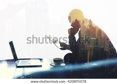 Double exposure silhouette of man skilled managing director is analyzing activities of the company by using touch pad and net-book. Thoughtful economist is reading news in network via digital tablet