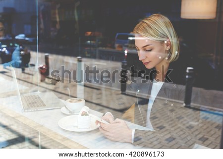 Woman is chatting via mobile phone with friends in social network,while resting after on-line learning via laptop computer during free time in coffee shop.Hipster girl is reading message on cell phone