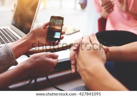 Closely of hand is holding cell phone with copy space screen for your advertising content. Two person are watching video in internet via mobile phone, while are sitting near open net-book on the table