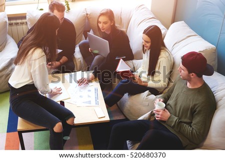 Group of young pupils is preparing for exams while sharing opinions sitting in coworking. Teamwork using computers, books and internet networking.Business professionals accounting income information