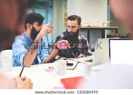 Leader tries to explain information to employee while sitting at the table and use laptop to prove his strategy. Two architects are planning their future building drinking coffee and discussing idea