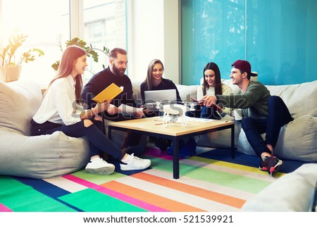 Creative staff of graphic design company brainstorming on informal meeting sitting in coworking office using modern drone.Students reading literature preparing for writing university coursework