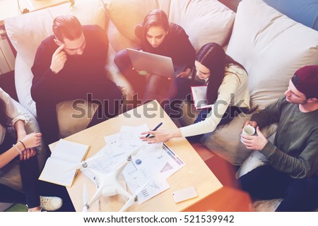 Professional team brainstorming sitting at the table of coworking space, reading reports accounting numbers of company clients while discussing ideas and concepts for successful business plan