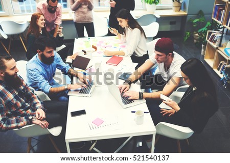Group of female and male IT professionals working on software development using modern devices while sitting at table. Skilled bloggers are copywriting for media web page typing on computer keyboard