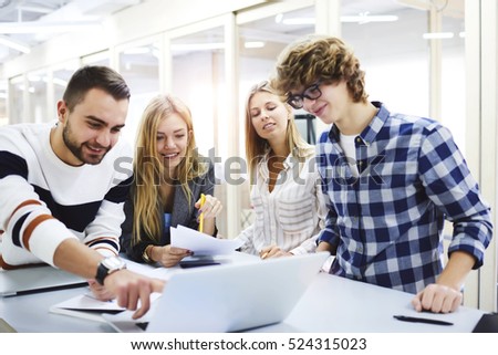 Students making a report for business teacher using modern computers,online information from web sites.Team works in friendly atmosphere smiling and joking feeling relaxed sitting in coworking space