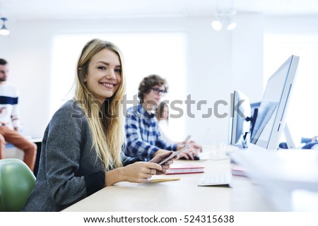 Female student of business school preparing makes report about using marketing strategies for increasing income of company sitting at lesson in good mood, smiling using technology and 5G connection
