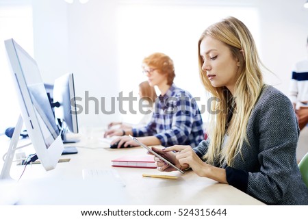 Creative female blogger typing text article while downloading music,sharing photo and video files with followers.Journalist making media research using social network via tablet  in coworking office
