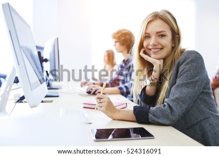 Young female student feeling ready to write exam testing and making individual tasks using technology computer and tablet connected to global network while smiling in university coworking space