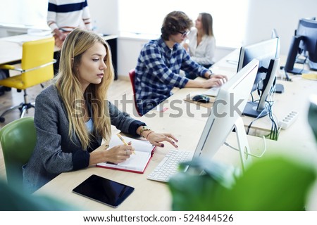 Female international student translating business article for upcoming exam using online programs and computer and fast 4G wifi connection during training lesson in modern university workshop
