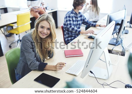 Young skilled pupil of software developing course smiling and working on individual task during programming lesson while sitting in front of computer using fast wifi in university modern workshop