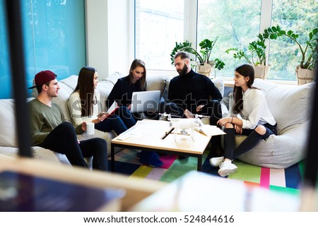 Yong freelance crew working hard on finding creative solution for internet social media tasks, sitting in coworking space using modern technology and consulting with skilled professional leader