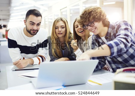 Male and female international students preparing for upcoming math exams reading  information from internet page via modern computer laptop having fun joking and smiling in university coworking space