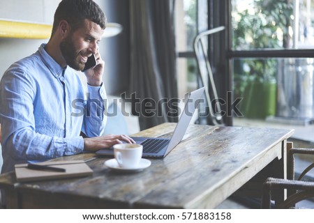 Successful male owner of business company talking with operator while making banking online consulting about cash remittance paying for bills using wireless internet and modern laptop in cabinet