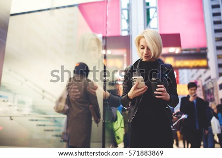 Attractive female traveller dressed in stylish casual wear sharing photos from journey to China in social networks and personal blog waiting from feedback while walking on street using 4G internet