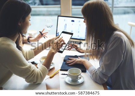 Creative female IT developers coding web site collaborating while working on design layout choosing right colors and multimedia on informal meeting in friendly atmosphere in coffee shop using devices