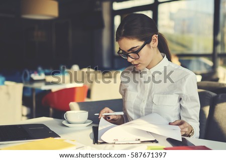 Skilled professional female administrative manager of coffee shop checking documentation for month before sending report to financier supervising working process and controlling stuff during revision