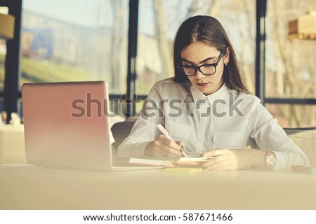 Creative female copywriter making text for advertising campaign and scripts for radio jingles and TV commercials noting best ideas to copybook before sending to ceo via email using laptop computer