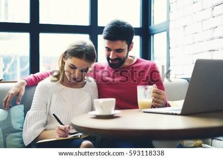 Beautiful couple of stylish hipster guys sitting in cozy coffe shop and spending time together having some tea in autumn day. Couple in love making planning list for weekend with things to do together