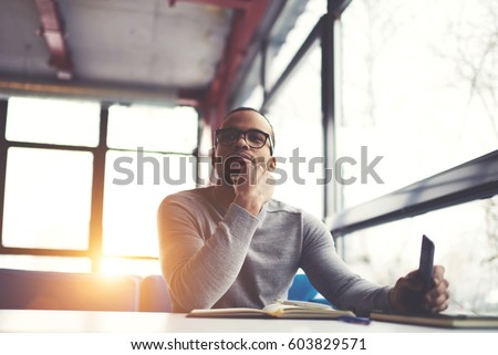 Pensive afro american handsome professional writer of popular articles in blog dressed in trendy outfit and glasses thinking over new story proofreading his script from notebook sitting in cafe