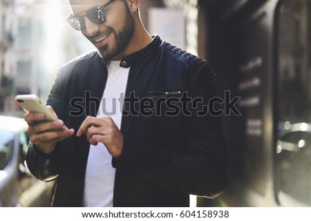 Close up portrait of smiling handsome trendy dressed hipster guy booking tickets on website of airplane company planning to visit foreign countries using smartphone and fast 4G internet connection