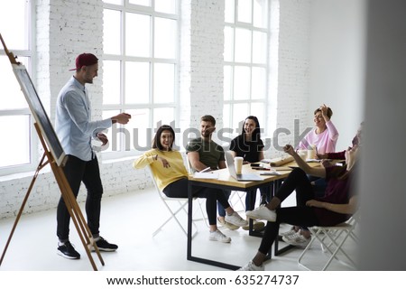 Skilled male marketing expert presenting creative ideas for advertising campaign to group of colleagues during meeting in office, coworkers sharing opinions during brainstorming session in good mood