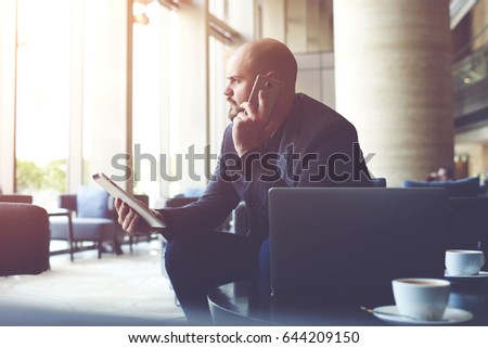 Serious man managing director of big prosperous company is holding touch pad and calling to manager to hear the explanation of why the client left a negative review about service on official website