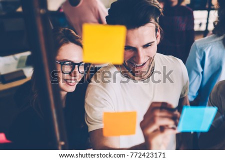 Cheerful male and female students planning working process using memo cards during brainstorming session, happy team members satisfied with having a lot of creative ideas writing on stickers