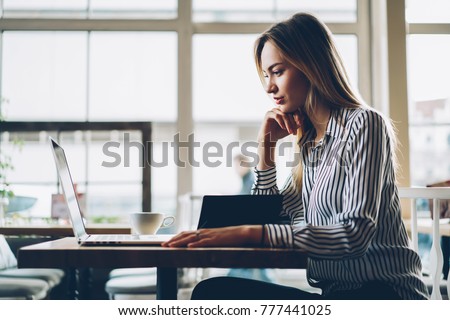 Side view of smart female copywriter concentrated on remote job preparing publication for web page sitting at netbook.Designer watching webinar to improve skills on laptop near copy space area