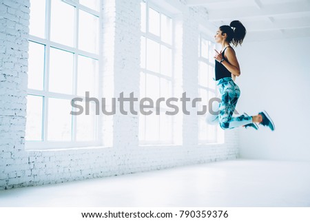 Young female in tracksuit jumping doing aerobics cardio exercises for losing weight and training strength,sportswoman doing leaps burning calories on pilates workout enjoying active lifestyle