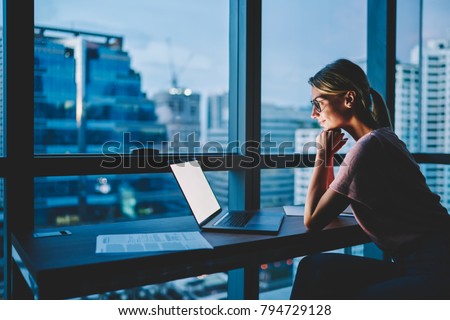 Positive hipster girl watching interesting movie online via high speed internet connection on modern laptop device spending evening leisure time in apartment.Blank copy space area of computer screen