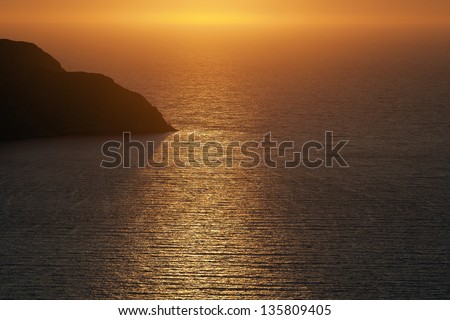 Sunset. Image shows the sun setting over the Mediterranean sea. The land belongs to Telendos island as can be seen from Kalymnos Island, one of the Dodecanese Greek islands in the Mediterranean sea.