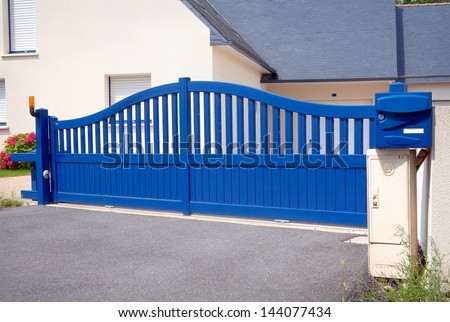 Blue Gates. New family house with blue automatic gates in front of garage door. Picture is taken in Brittany , France and blue color is traditional. Automatic gate, also cantilever gate.