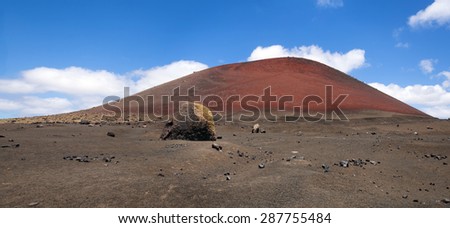 Montana Roja (Red mountain) with a large boulder ex-pulsed from the volcano. Typical volcanic landscape of Lanzarote island. Canary islands, Spain.