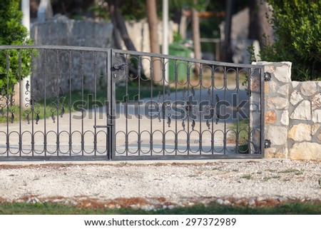 detail of a new metal gate on a driveway, attached to the pillar of a low stone wall