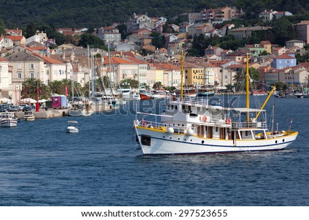 colorful waterfront in small port town of Mali Losinj on the Croatian island of Veli Losinj; lively sea traffic with many boats in background and small tourist cruiser in front