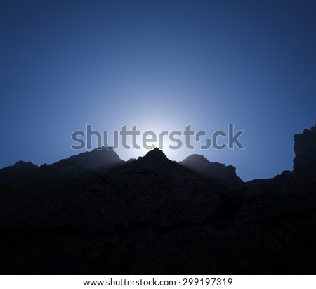 mountains at sunrise; the sun is rising up behind one of the peaks in a mountain ridge;\
silhouette of huge mountain massif  in the moment of the sunrise
