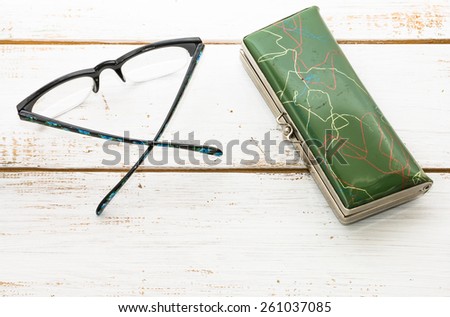 Black glasses and green spectacle case  on vintage wooden background