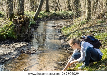 Young woman hiker with backpack by the river in the spring forest, outdoor activities and leisure
